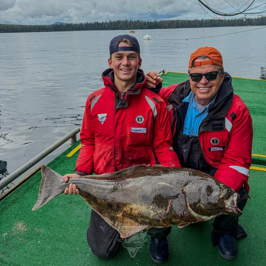 Two anglers kneeling on the boat deck behind a big halibut.