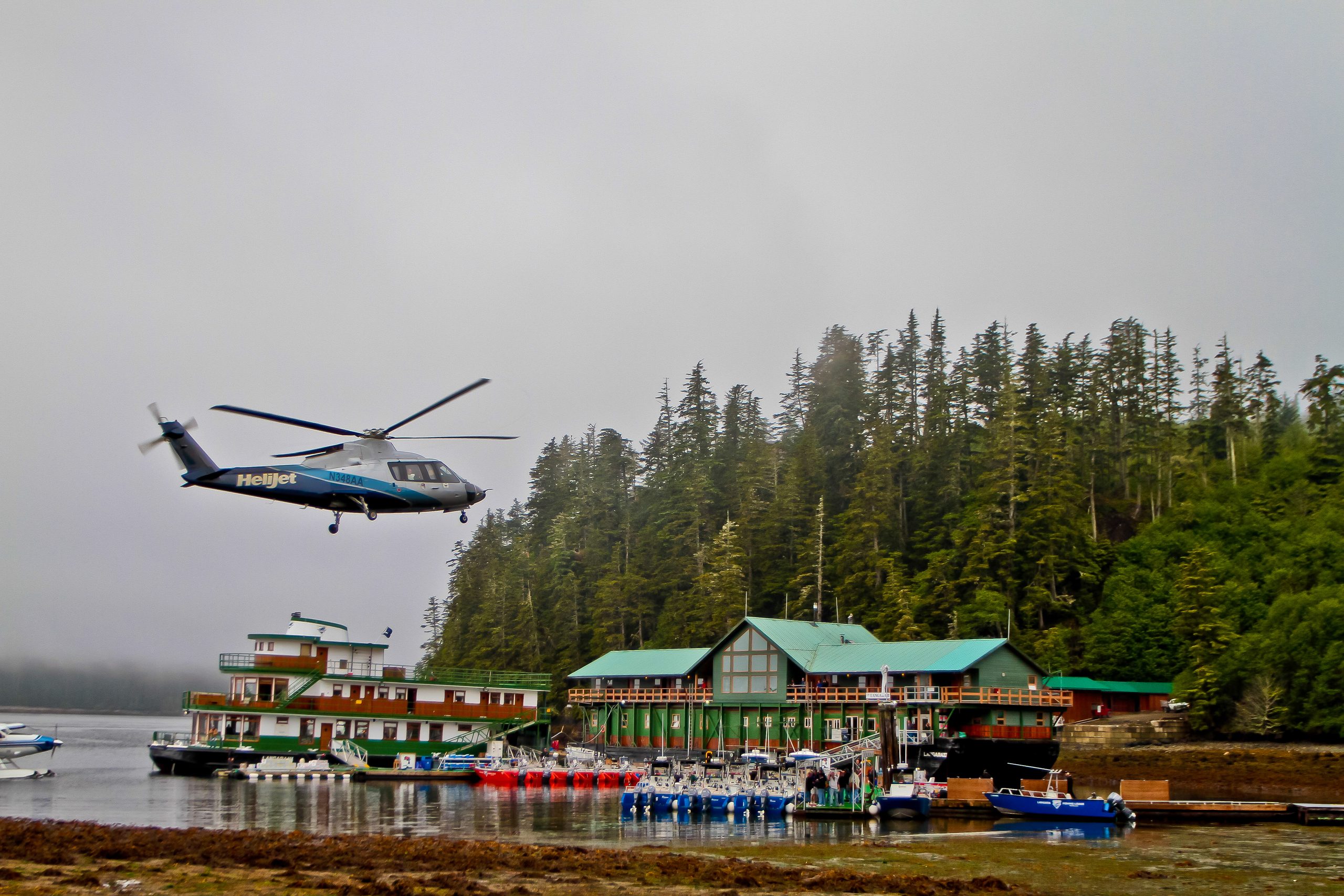 A helicopter arriving at Langara Fishing Lodge, the lodge and its boats below the forest.