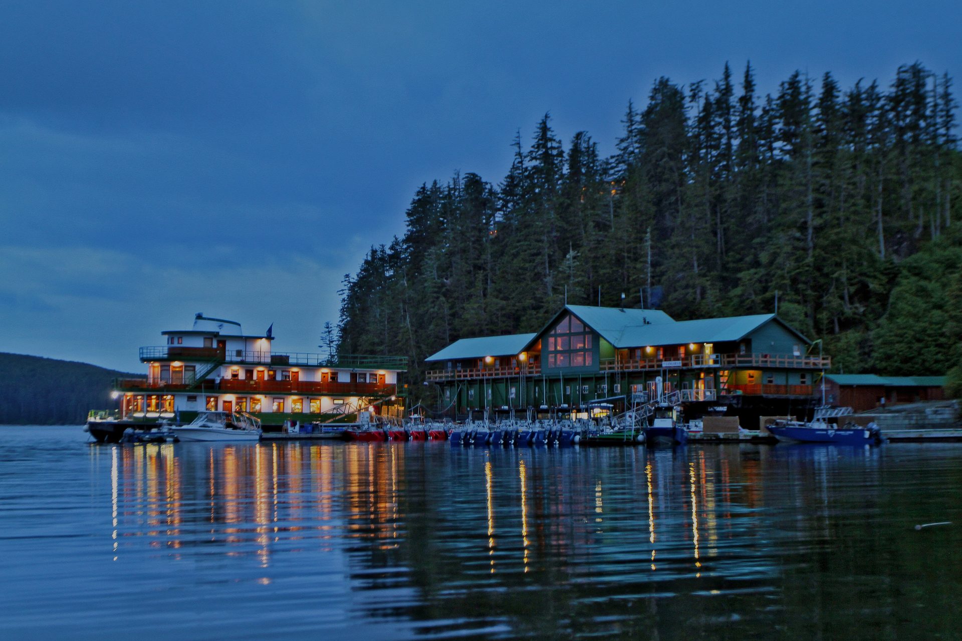 Langara Fishing Lodge lit up at dusk, its lights reflected in the calm water.